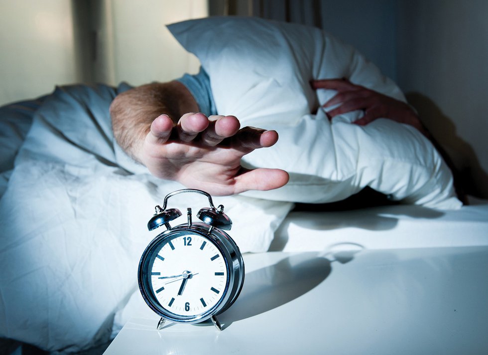 Waken man stretching hand to turn off alarm clock