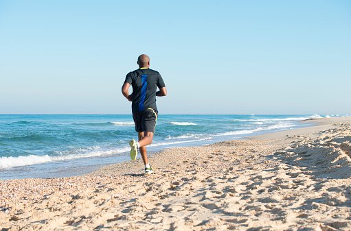 Back view of a young man running outdoors in the beach.