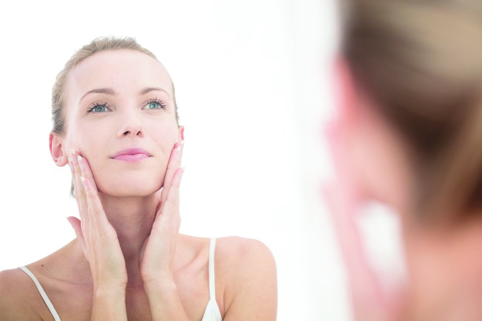 Young woman looking in mirror, applying moisturiser to face