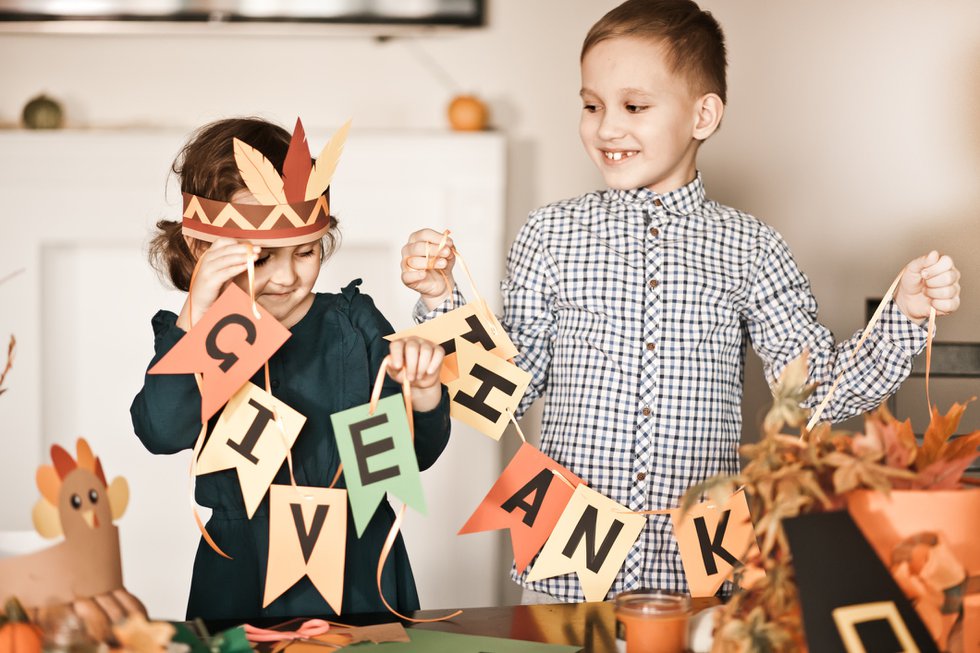 Kid holding paper garland with text Give thanks. Children decorating living room for celebrating Thanksgiving day.