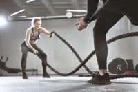 Athletic woman doing battlerope exercise with personal trainer at gym