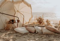 Picnic setup on the beach with pillows and lush florals