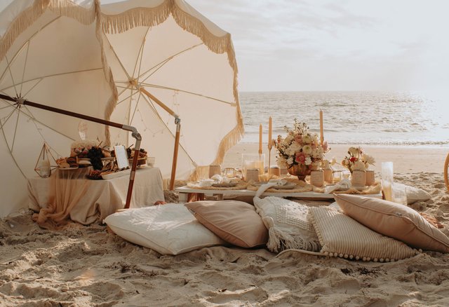 Picnic setup on the beach with pillows and lush florals